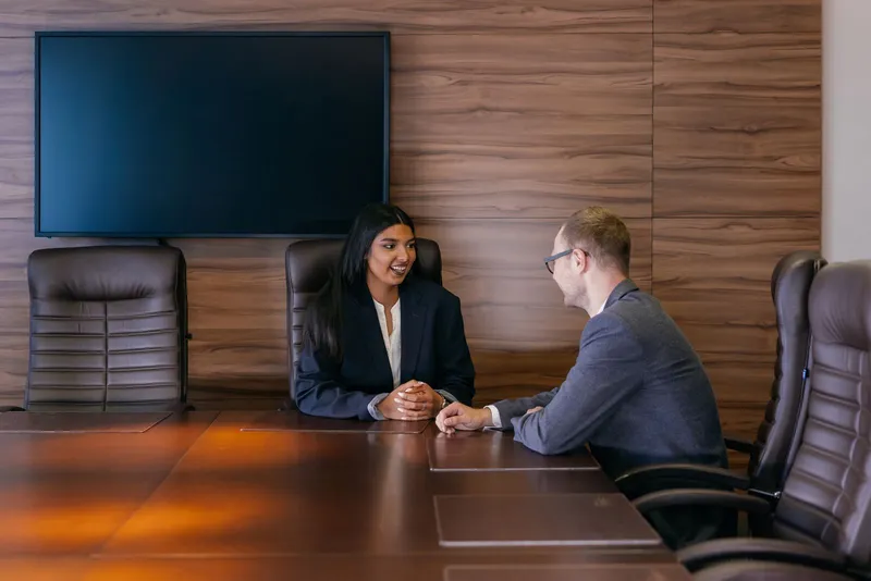 Two people in discussion across a boardroom table