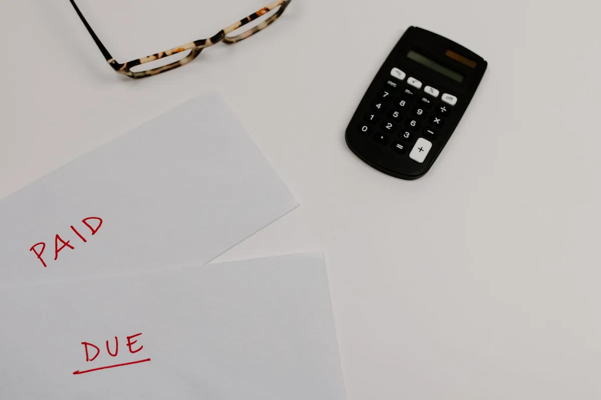 Papers marked paid and due beside a calculator and a pair of glasses
