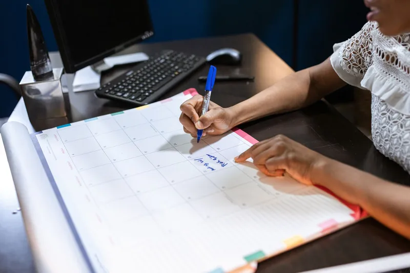 A person writing notes on a large desk calendar