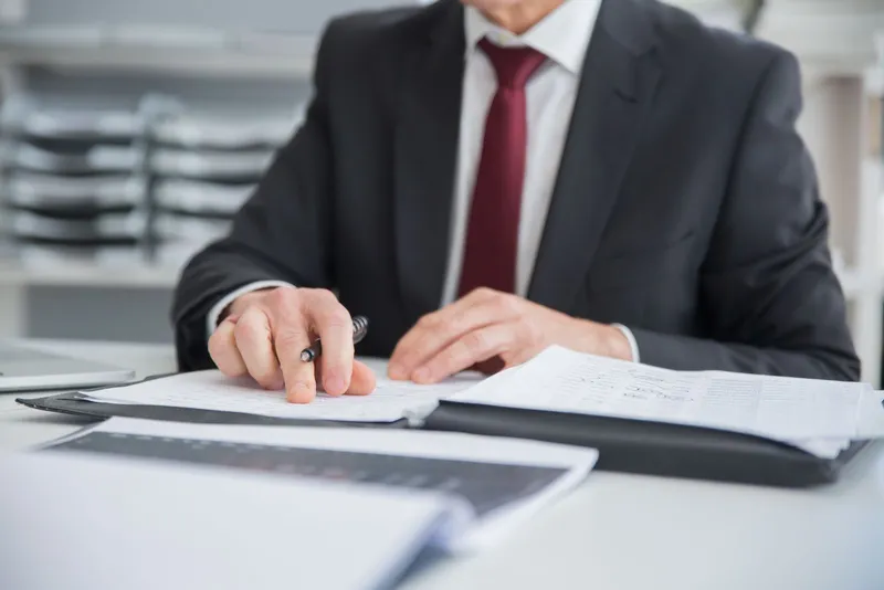 A man in a suit reading through printed documents at a desk